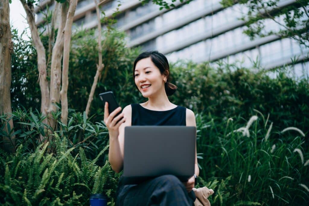 Woman working with laptop outdoors in urban office park, surrounded by green plants.