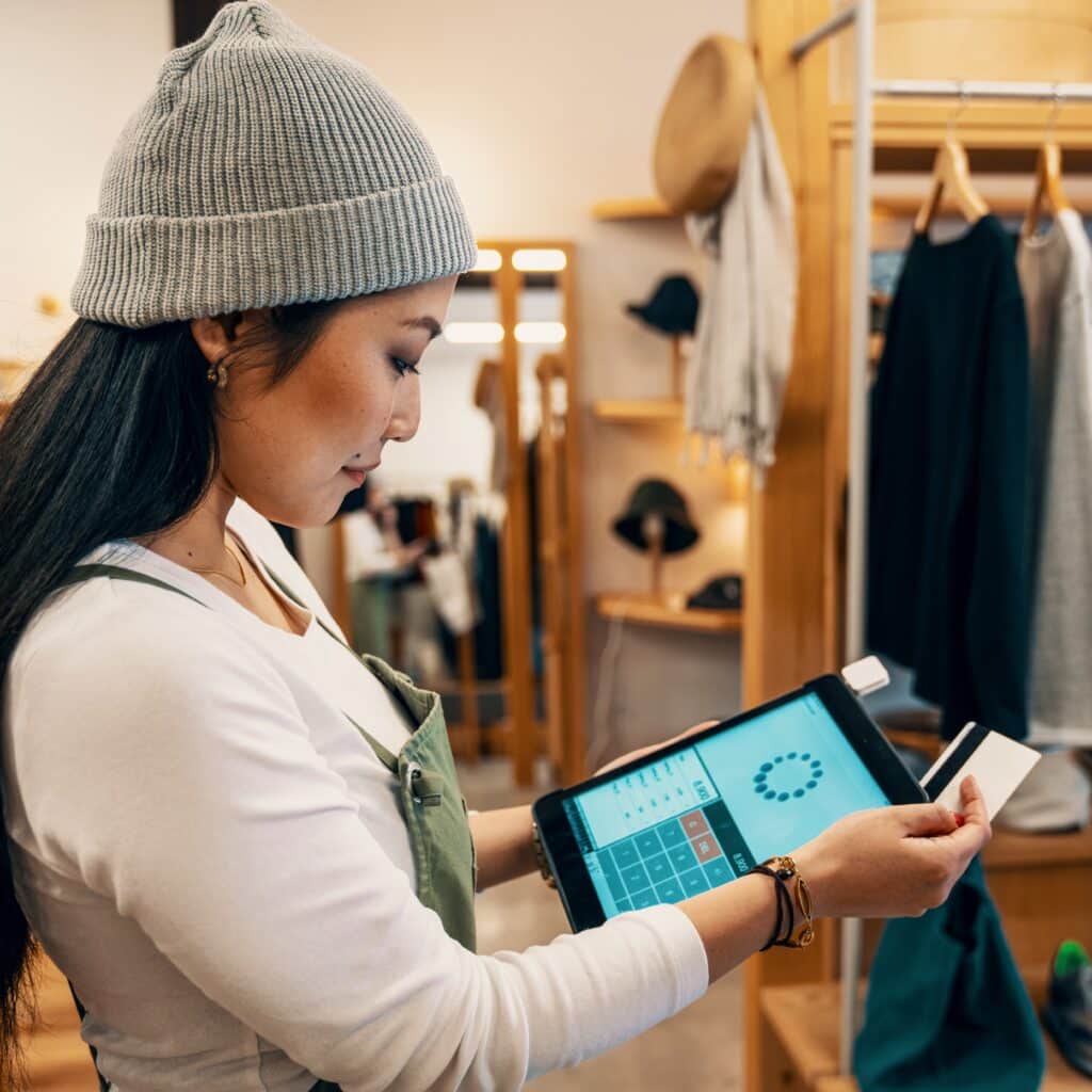 Shop clerk in a clothing boutique taking a credit card payment on a digital tablet.