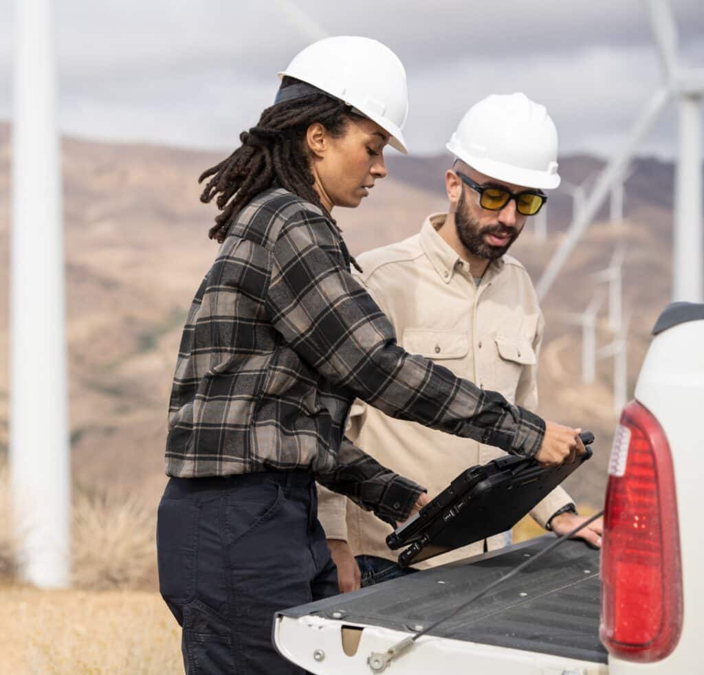 Field engineers using a laptop on truck tailgate to review data after inspection of turbines on a wind farm.