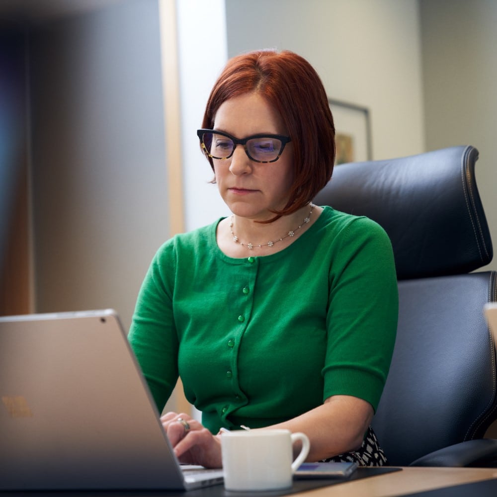 A person sits at a laptop next to a cup of coffee.